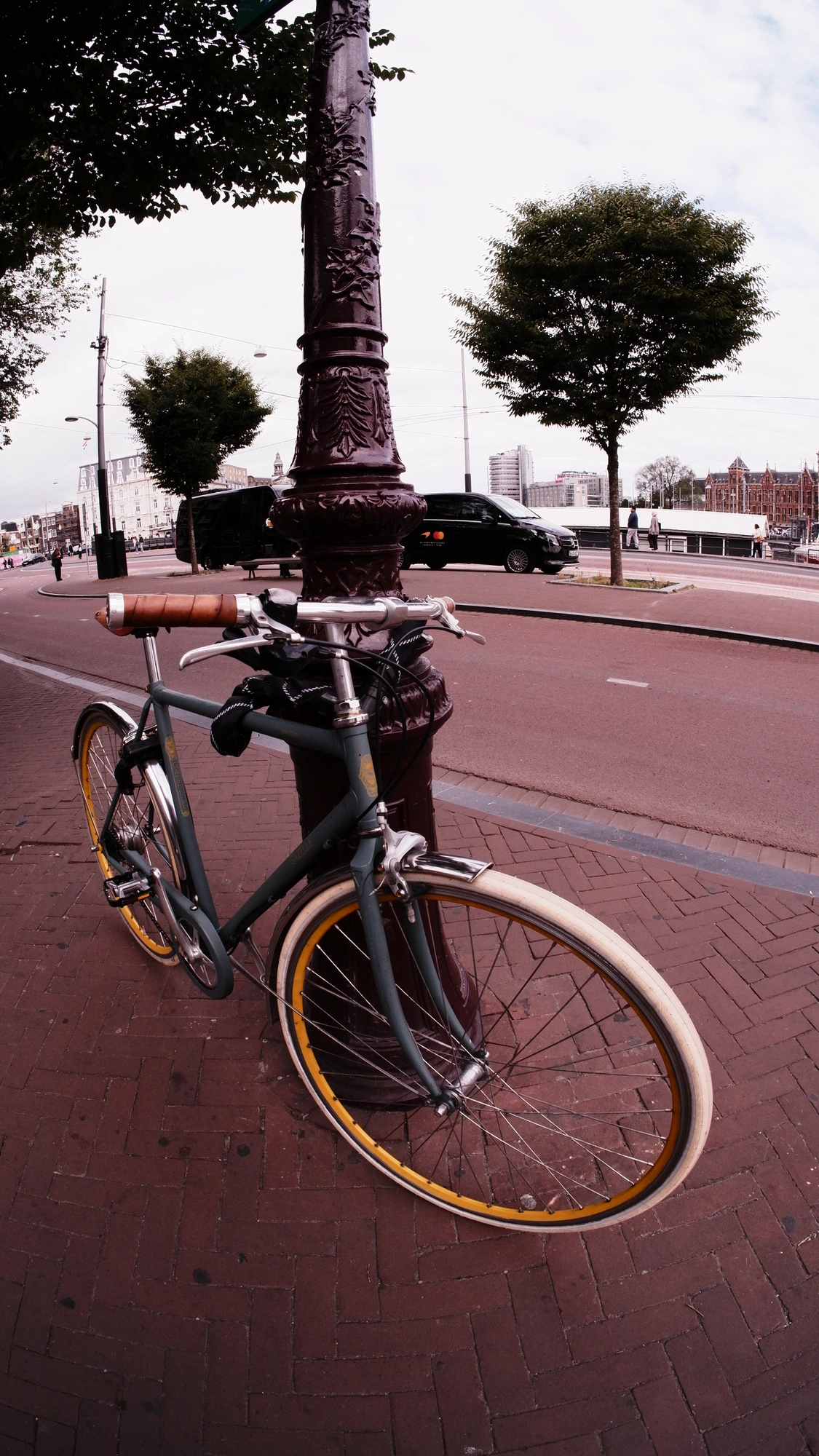 Green bike with yellow rims parked against old style street pole