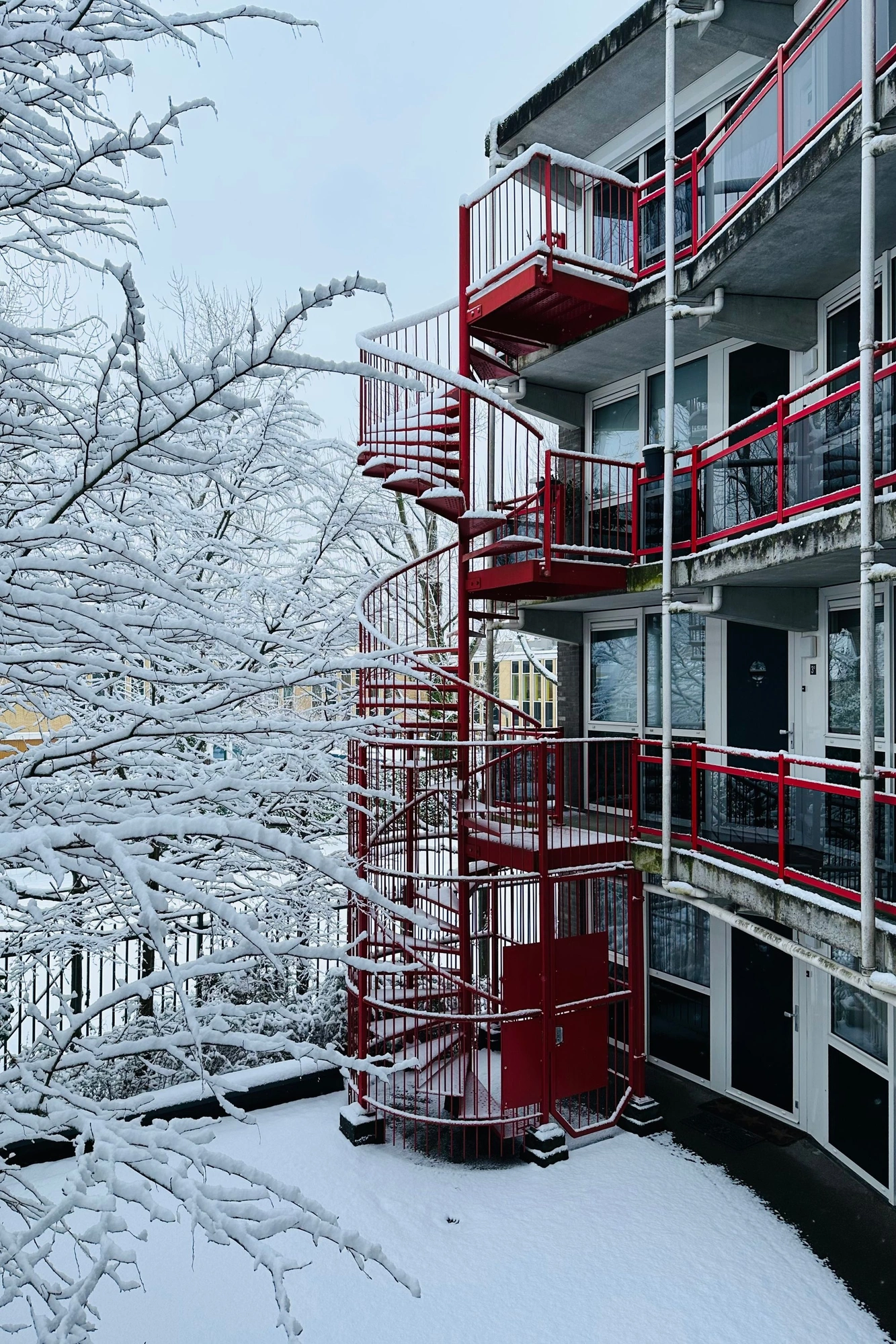 2026-01-03 - i16 - color - NL - Apartment building with red staircase and snow-covered tree