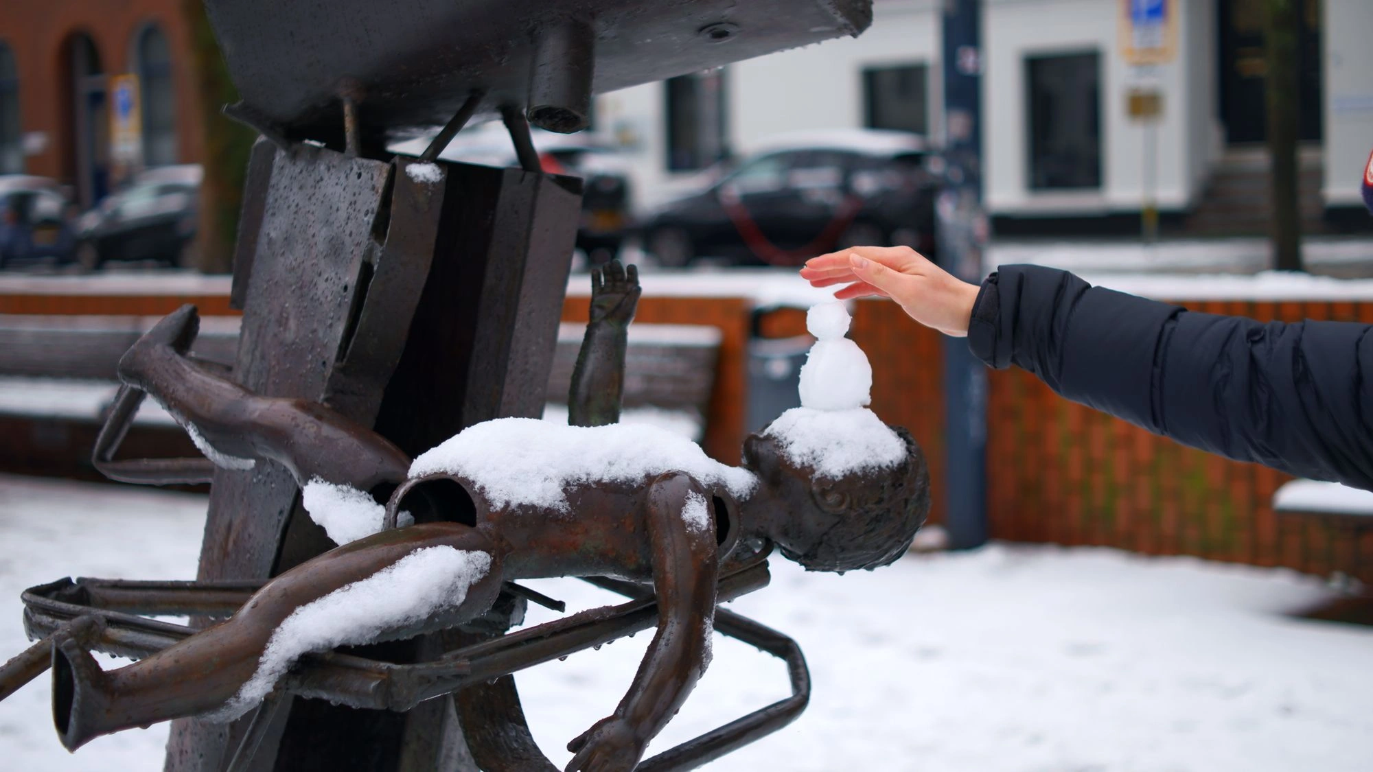 2026-01-04 - xt35 - color - NL - Rotterdam - Hand touching the touch of a snowman on to of an abstract sculpture of a child