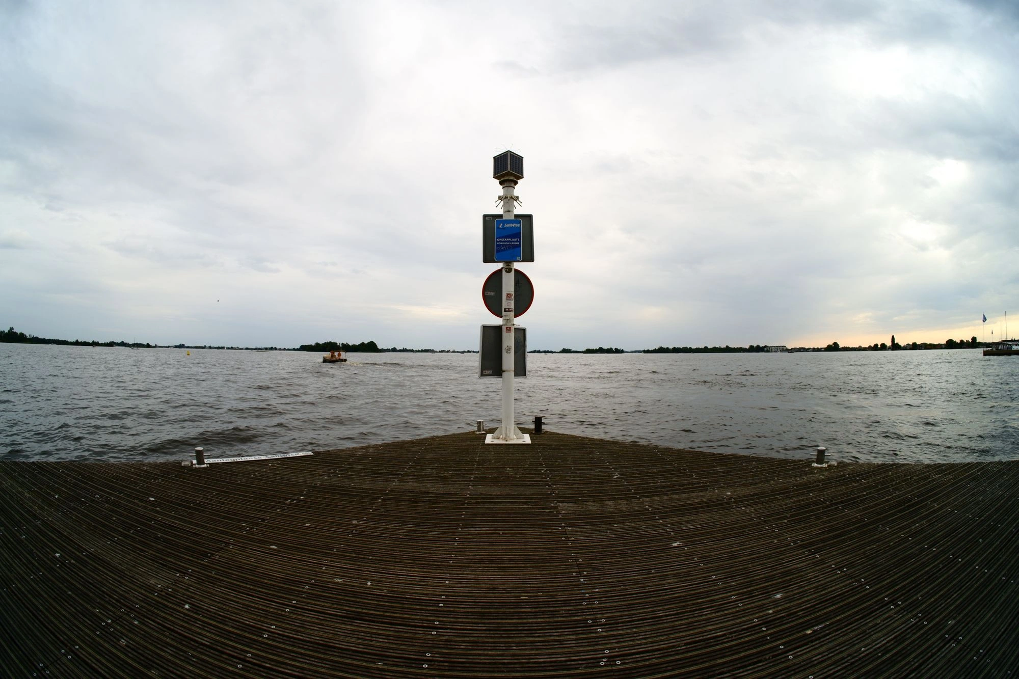 Sign post at the edge of pier with water and trees in the distance