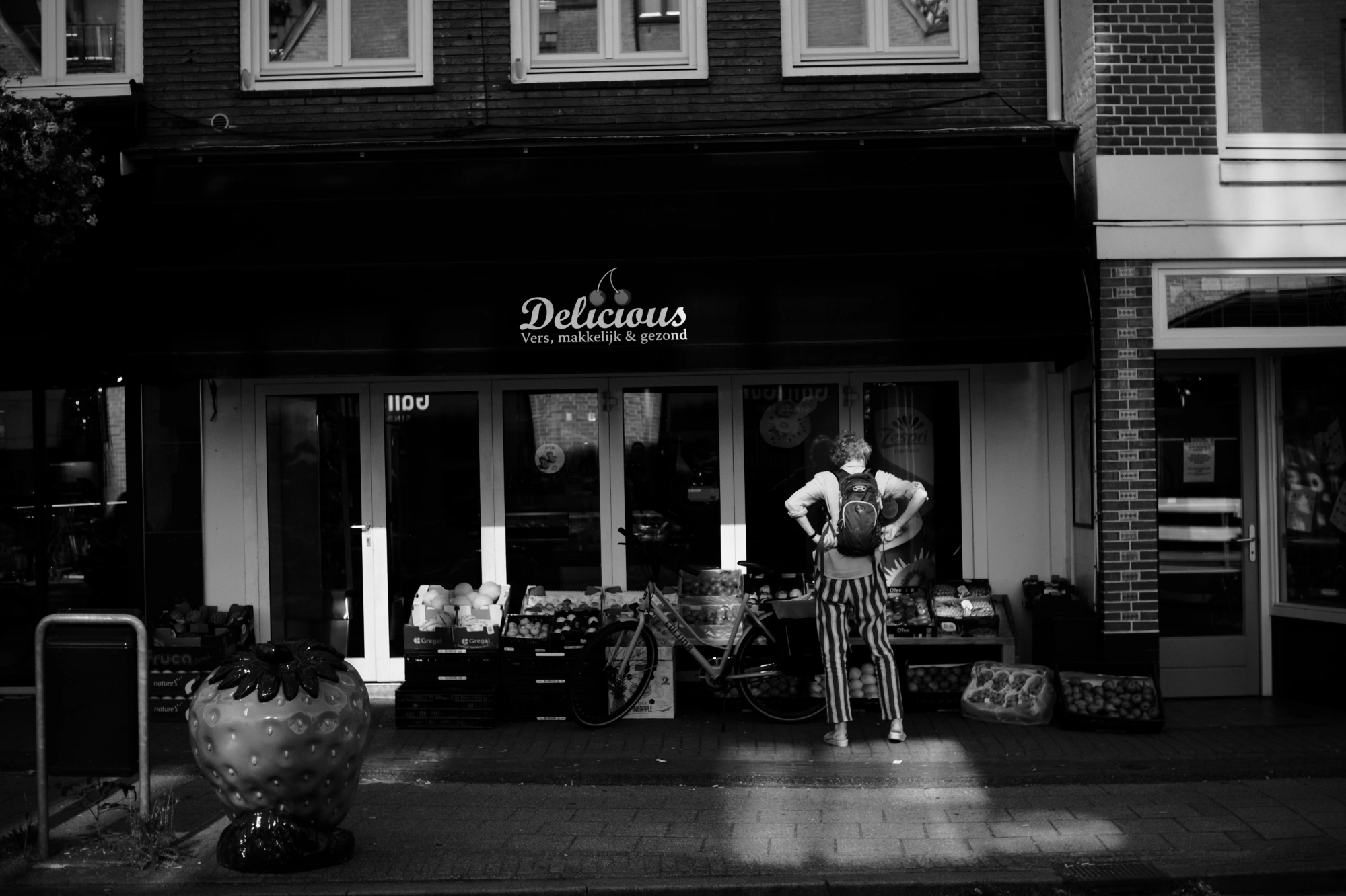 2023-09-09 - xt35 - bw - NL - Person standing in front of green grocer