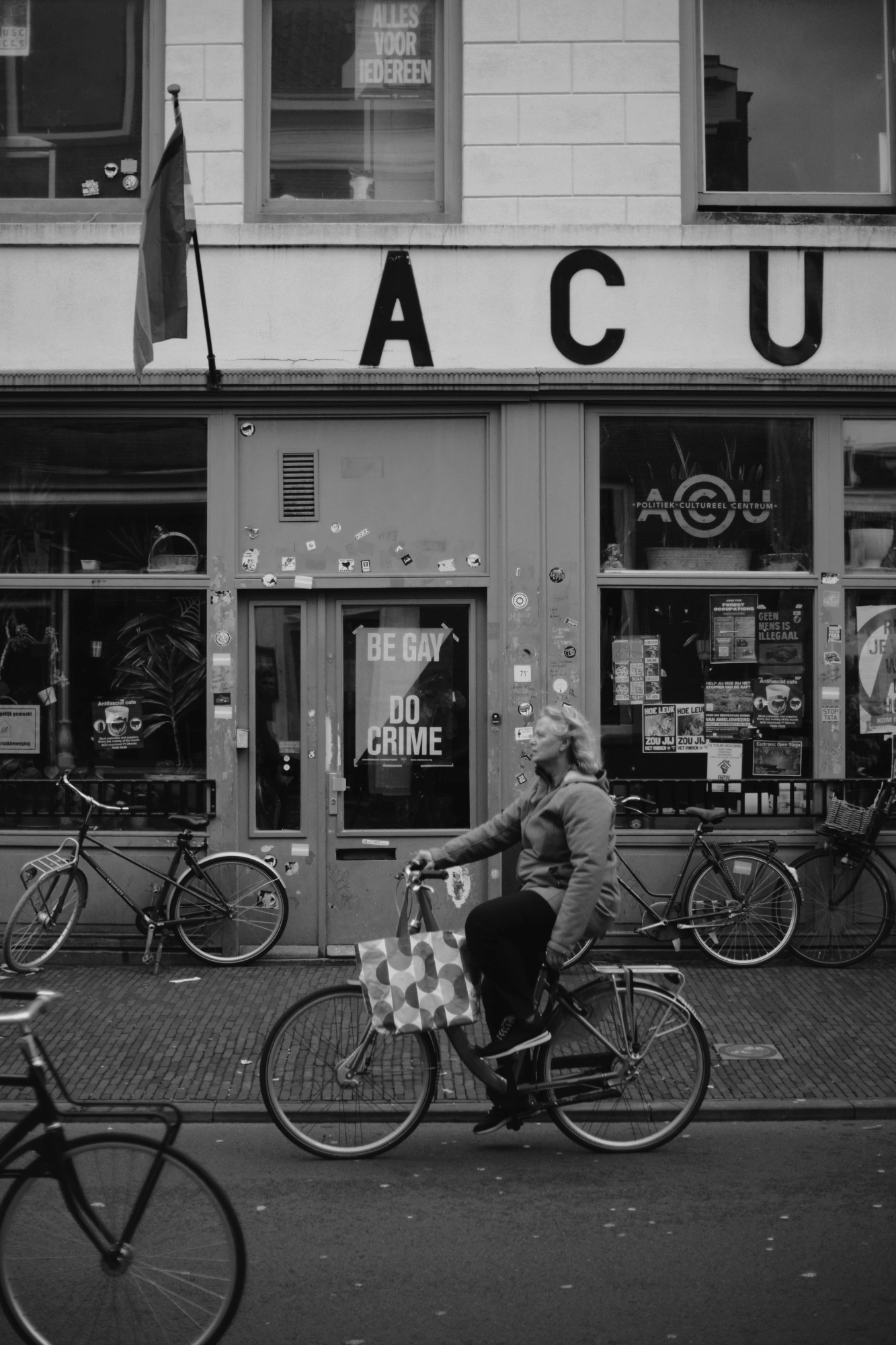 2024-01-21 - xt35 - bw - NL - Person cycling in front of sign that says 'Be gay do crime'
