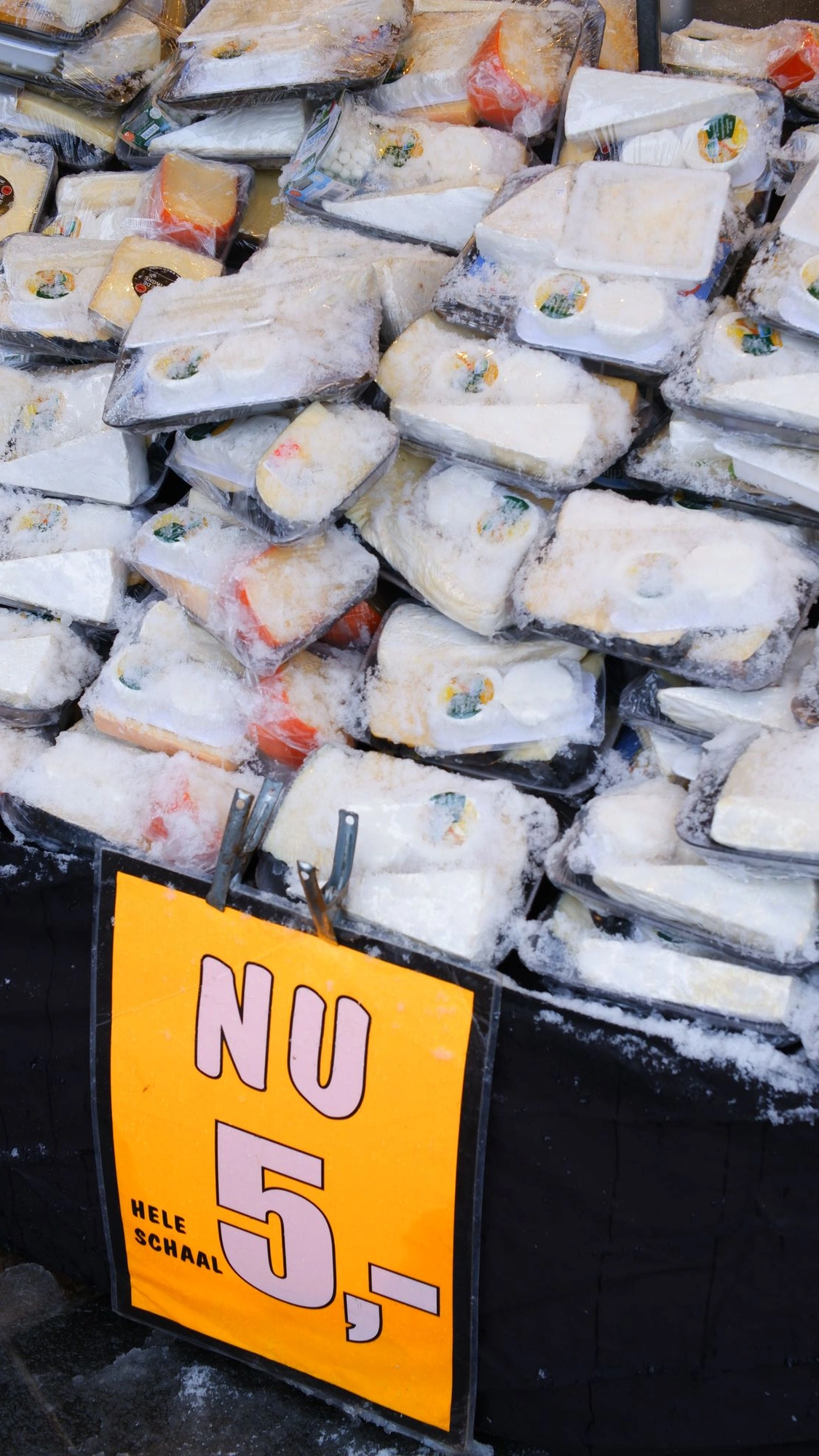 Cheese covered in snow with a sign that says "Nu 5,- Hele Schaal".J