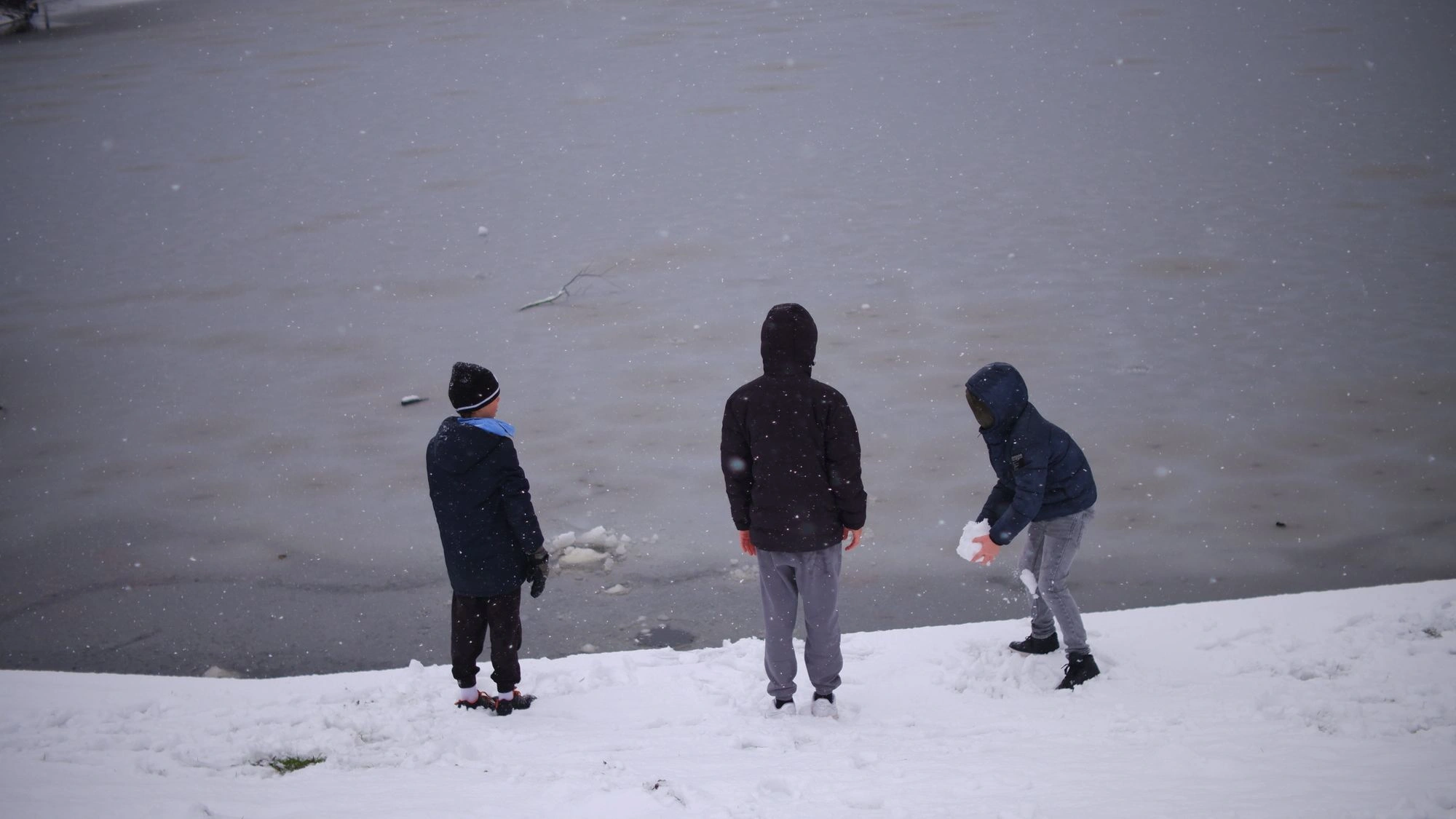 Kids throwing snow into the frozen lake.J