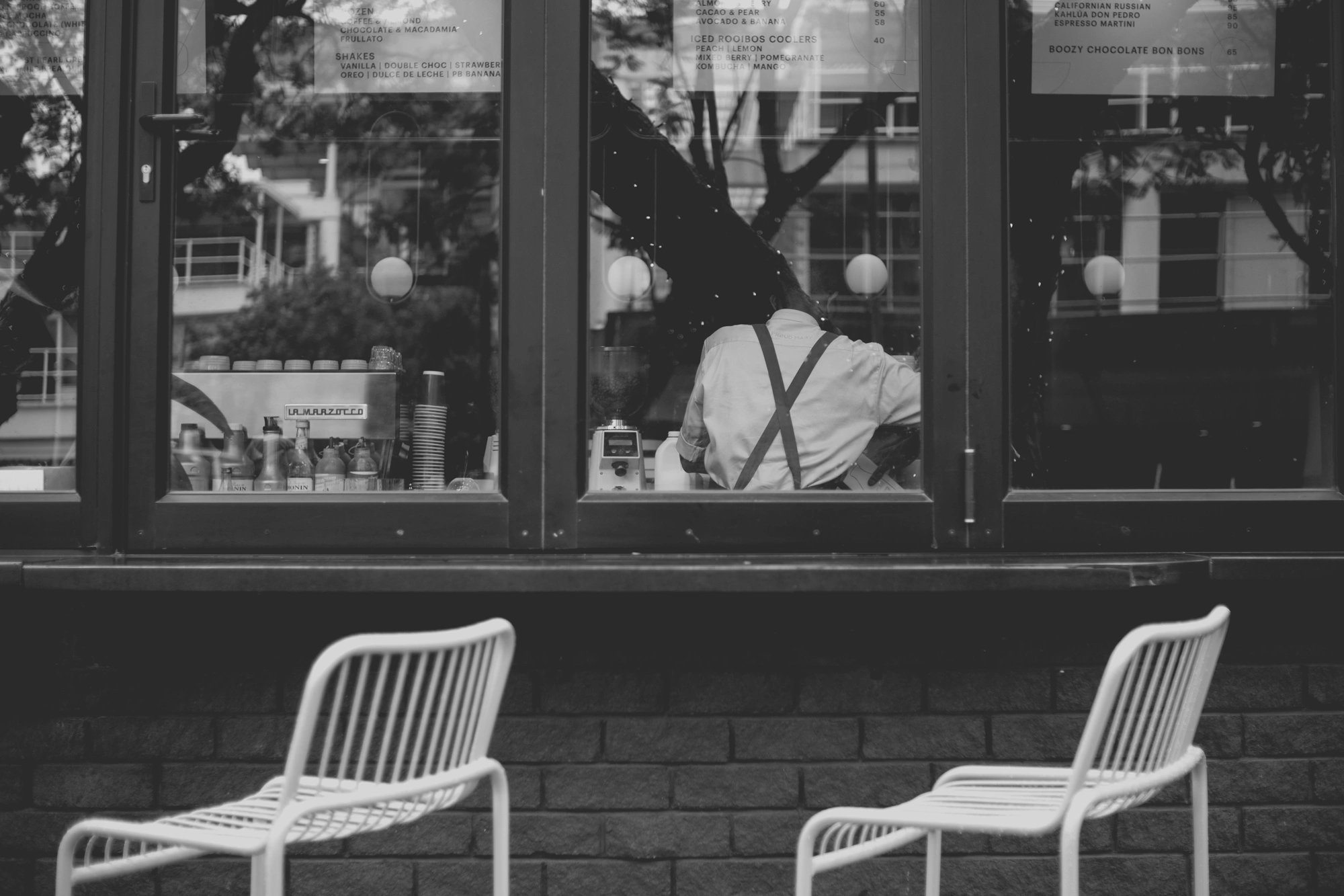 2021-12-19 - Rosebank, Johannesburg - Barrista working as seen through coffee shop window.j