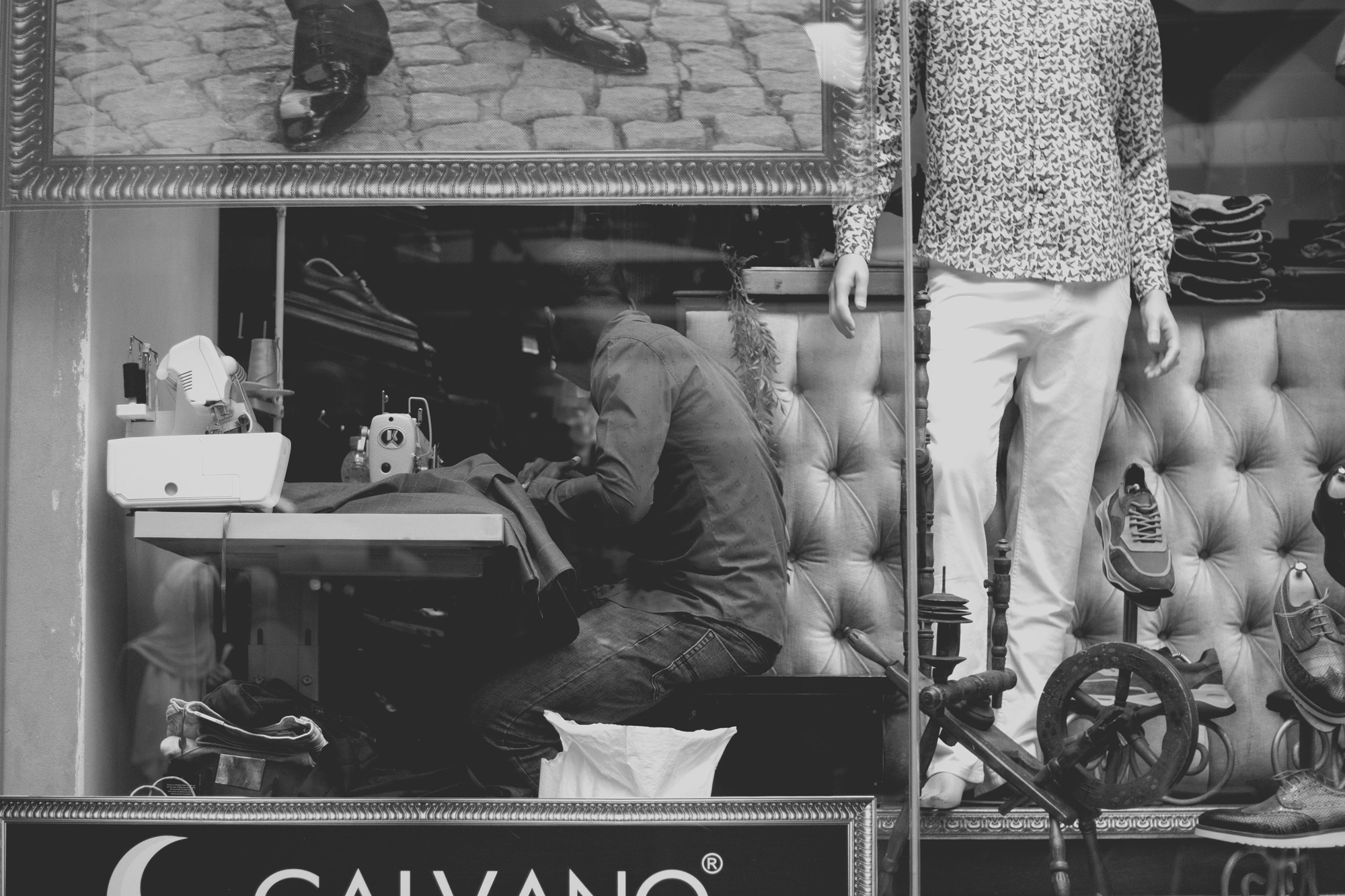 2021-12-19 - Rosebank, Johannesburg - Tailor working as seen through store window.j